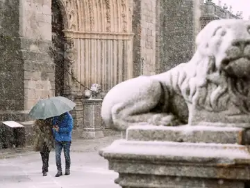 Dos personas se protegen de la nieve junto a los leones de la catedral de Ávila