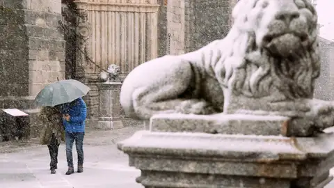 Dos personas se protegen de la nieve junto a los leones de la catedral de Ávila Dos personas se protegen de la nieve junto a los leones de la catedral de Ávila