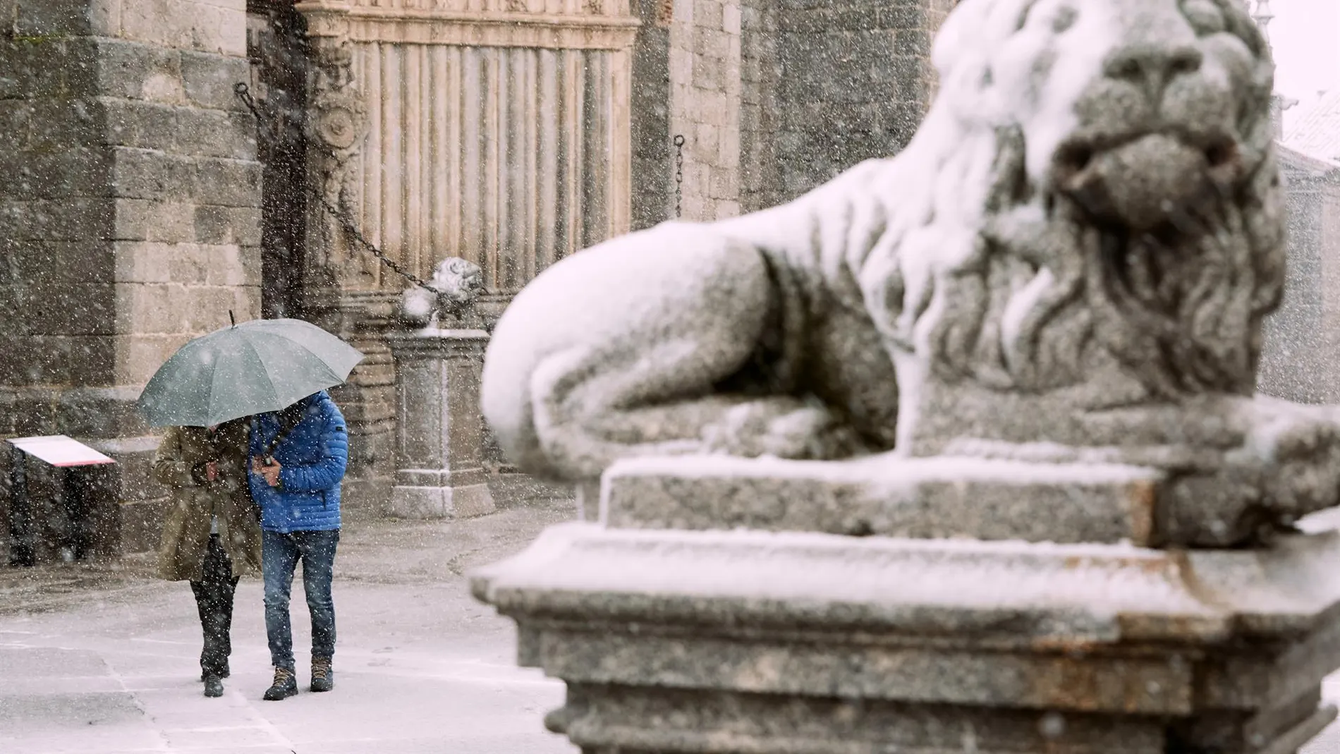 Dos personas se protegen de la nieve junto a los leones de la catedral de Ávila