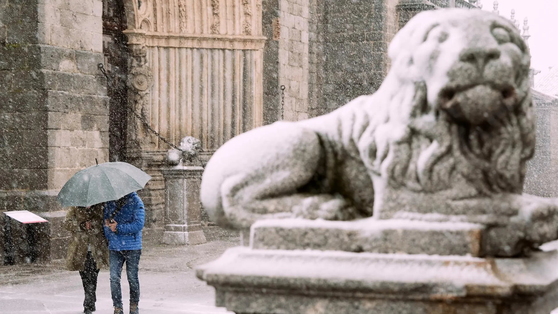 Dos personas se protegen de la nieve junto a los leones de la catedral de &Aacute;vila