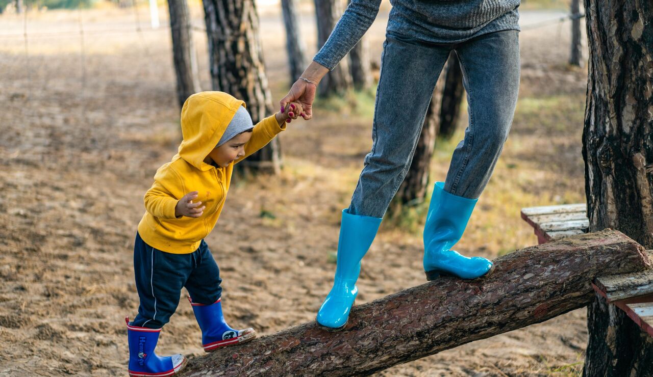 Un niño de la mano de su madre juega sobre un tronco.