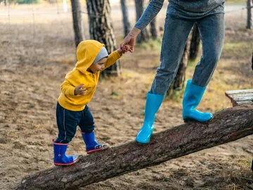 Un niño de la mano de su madre juega sobre un tronco. Un niño de la mano de su madre juega sobre un tronco.