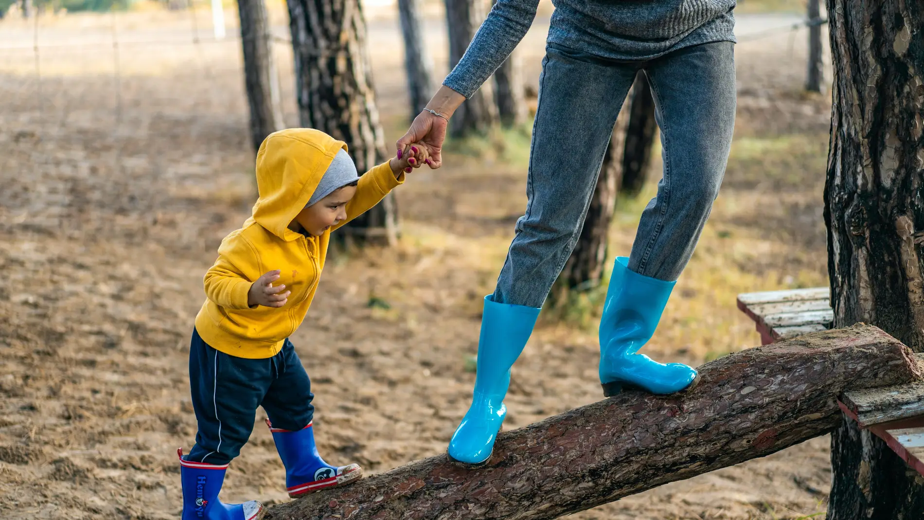 Un niño de la mano de su madre juega sobre un tronco.