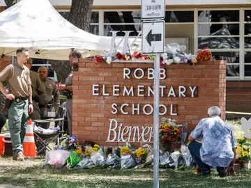 Un hombre se arrodilla junto a un monumento de flores en el lugar de un tiroteo masivo en la Escuela Primaria Robb