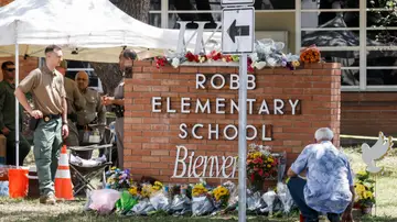Un hombre se arrodilla junto a un monumento de flores en el lugar de un tiroteo masivo en la Escuela Primaria Robb