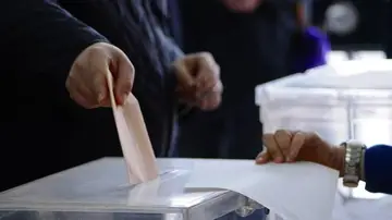 Una persona deposita su voto en la urna de una mesa electoral