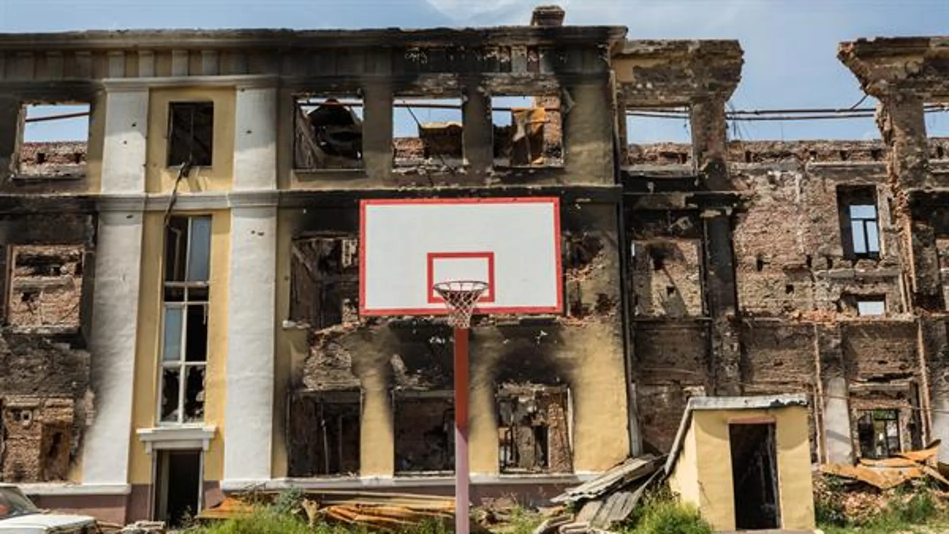 Una canasta de baloncesto frente a una escuela destruida