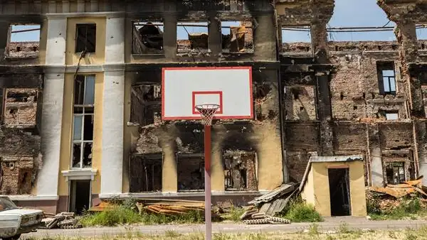 Una canasta de baloncesto frente a una escuela destruida Una canasta de baloncesto frente a una escuela destruida
