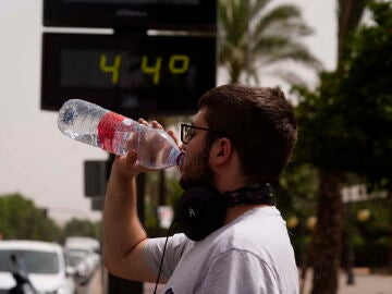 Un joven bebiendo agua frente a un termómetro con altas temperaturas