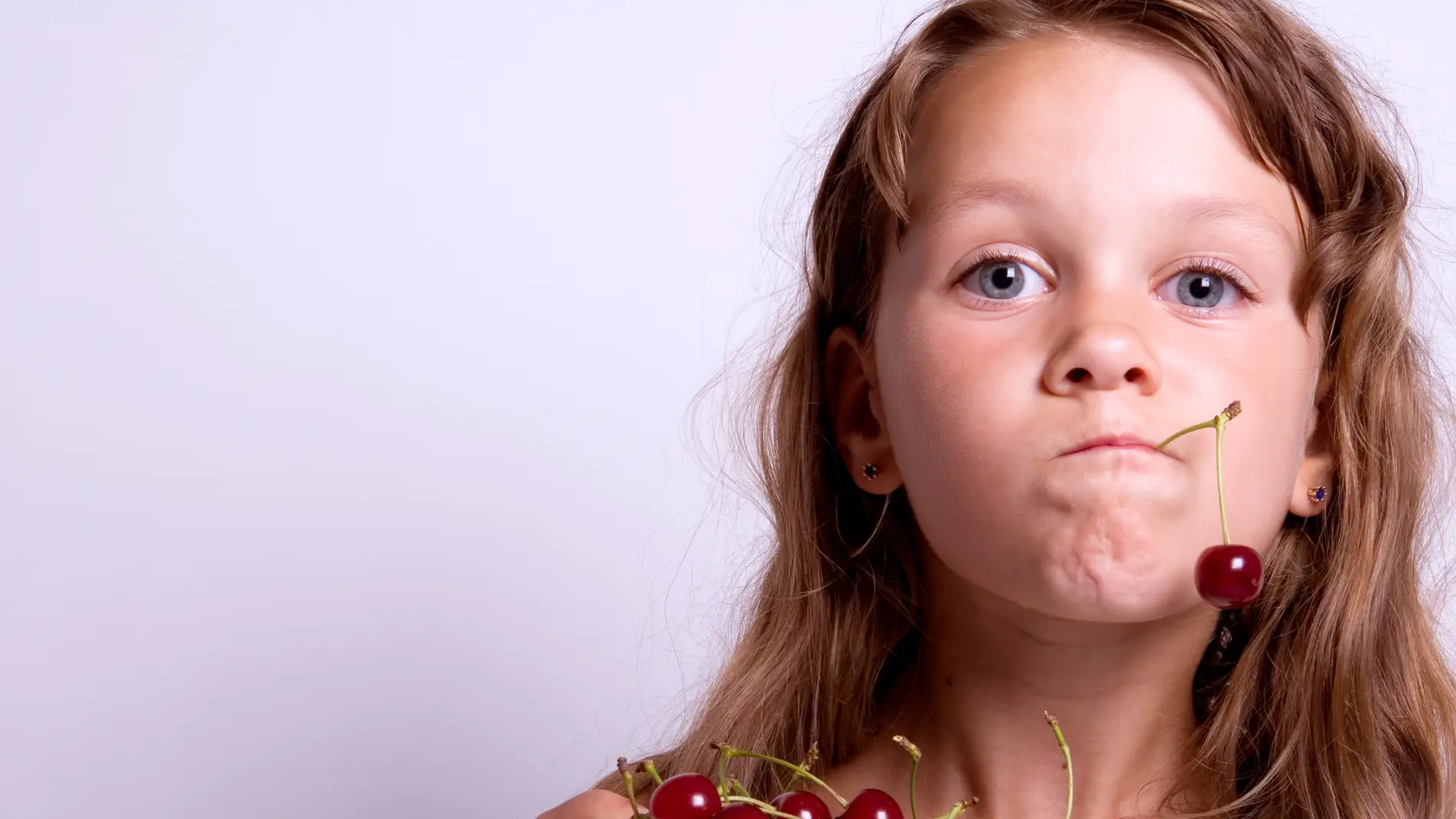 Una niña comiendo cerezas.