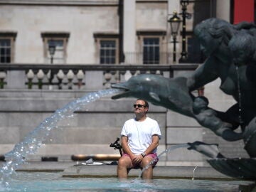 Un hombre descansa bajo una fuente en Trafalgar Square, en Londres