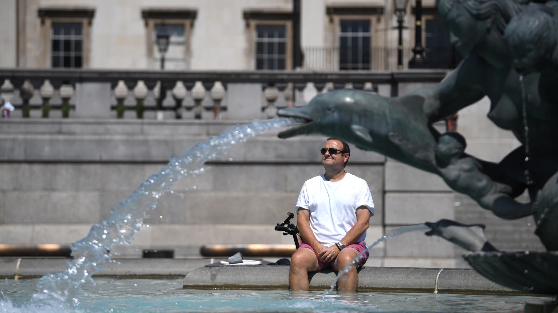 Un hombre descansa bajo una fuente en Trafalgar Square, en Londres