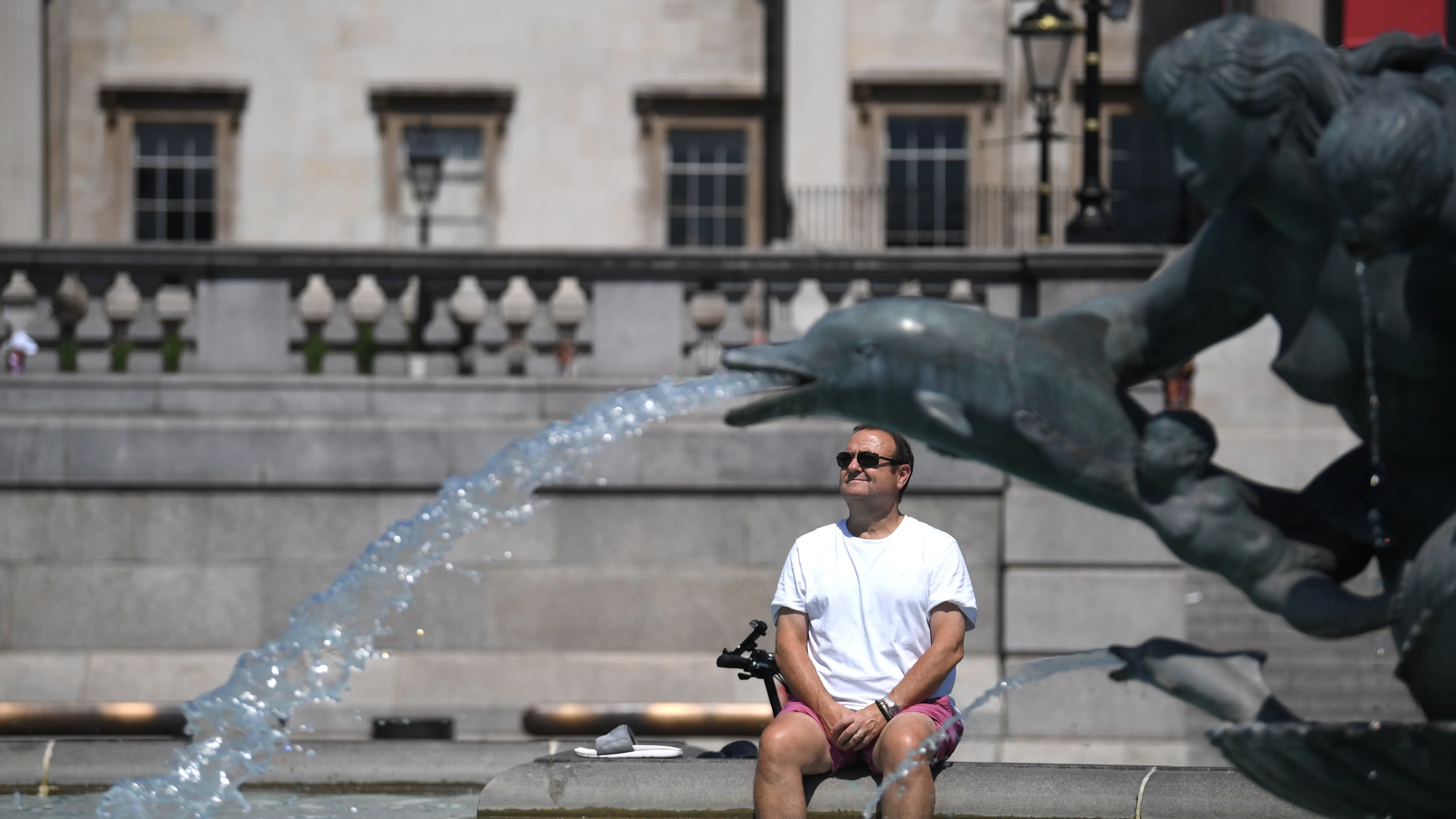 Un hombre descansa bajo una fuente en Trafalgar Square, en Londres Un hombre descansa bajo una fuente en Trafalgar Square, en Londres