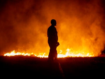 Un vecino ante las llamas mientras colabora en las labores de extinción del incendio de Cures, en Boiro, A Coruña, en la madrugada de este sábado.