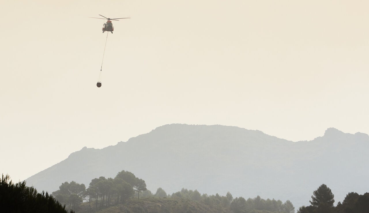 Un helicóptero se dirige cargado con agua hacia el frente del incendio forestal declarado en la Vall d'Ebo (Alicante).