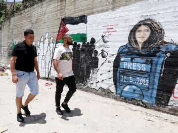 Dos palestinos caminan frente a un mural de la periodista Shireen Abu Akleh