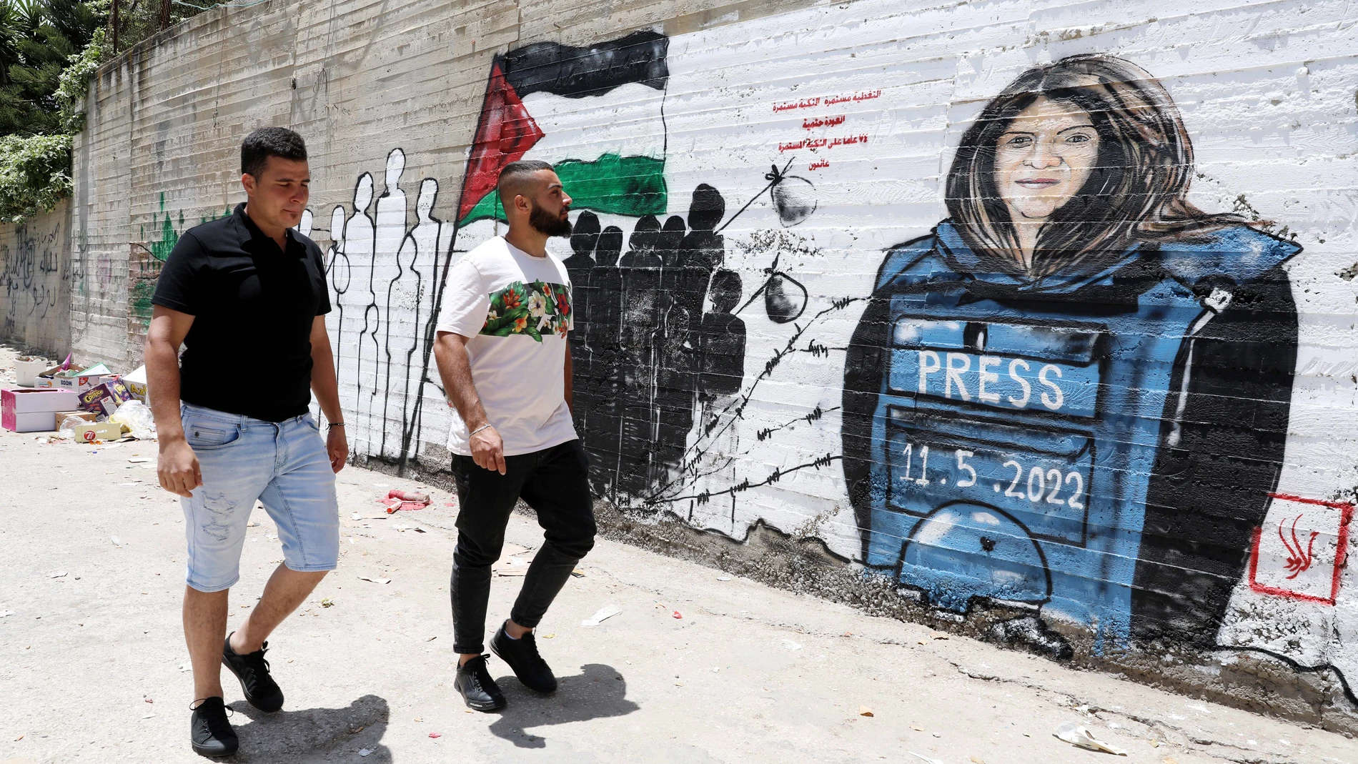 Dos palestinos caminan frente a un mural de la periodista Shireen Abu Akleh