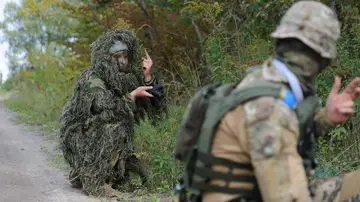 Un instructor militar vestido con camuflaje ghillie y sosteniendo un arma participa en un entrenamiento militar para civiles organizado por la organización política ucraniana