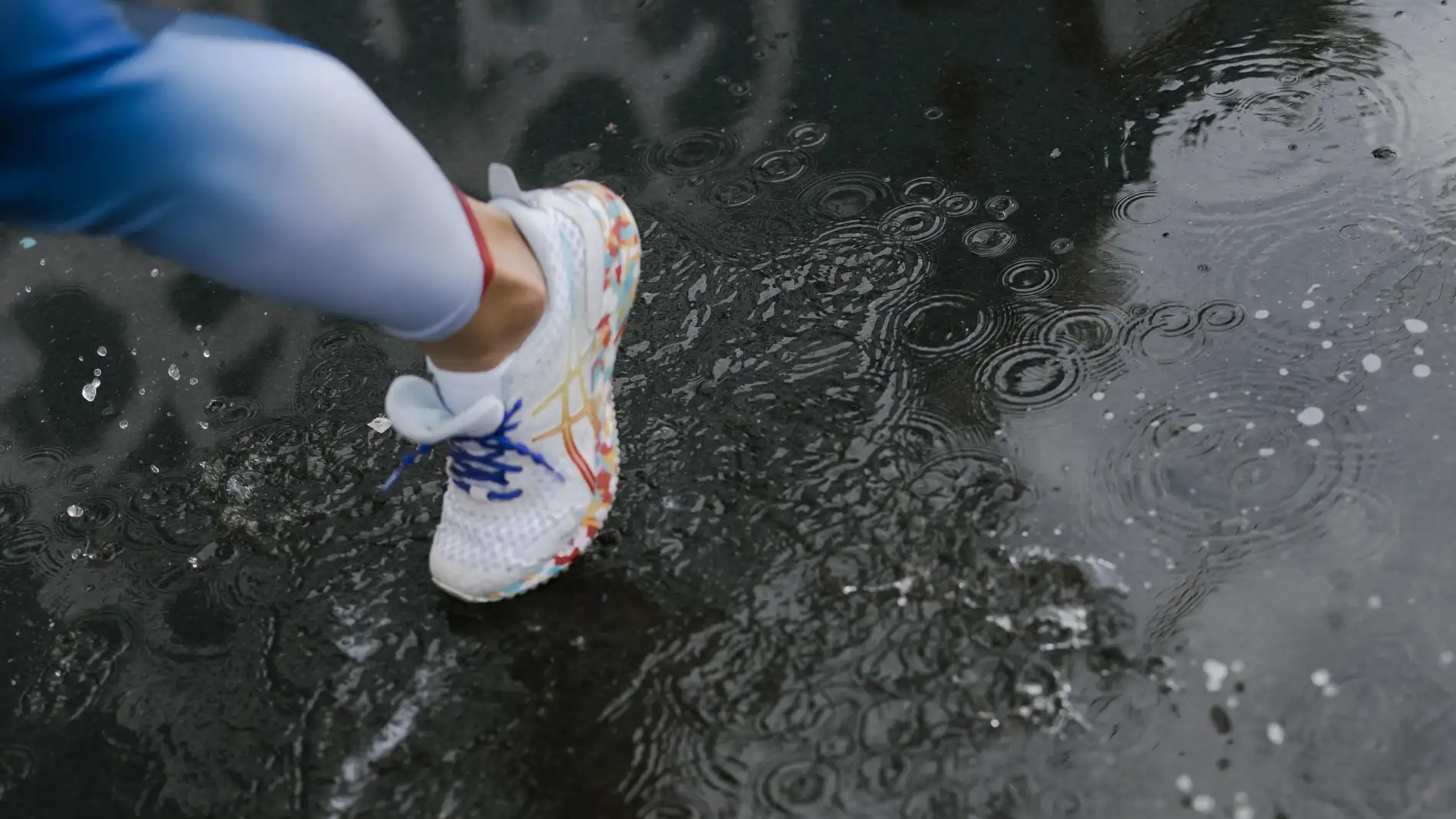 Una persona con calzado de deporte camina sobre el suelo mojado.