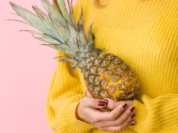 Una mujer sujeta una piña con las manos. Una mujer sujeta una piña con las manos.