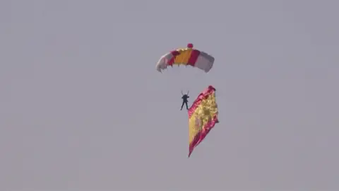 El paracaidista, con la bandera española, durante el Día de la Hispanidad El paracaidista, con la bandera española, durante el Día de la Hispanidad