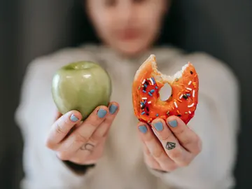 Una mujer sostiene una fruta y un dulce Una mujer sostiene una fruta y un dulce