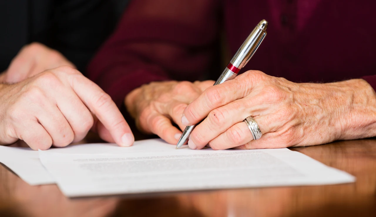 Una persona mayor firma un documento