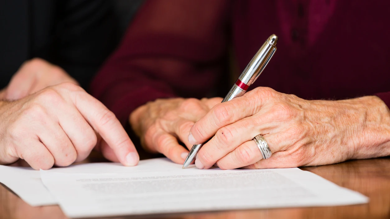 Una persona mayor firma un documento Una persona mayor firma un documento
