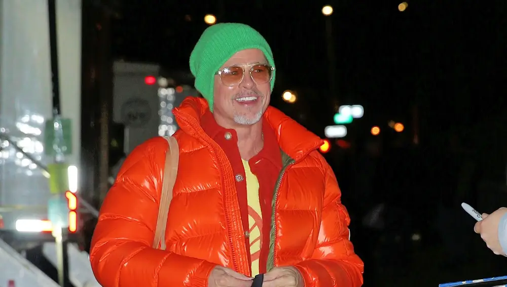 Brad Pitt con un plumas naranja y gorro verde flúor