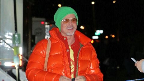 Brad Pitt con un plumas naranja y gorro verde flúor