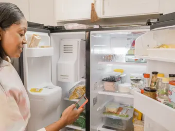 Una mujer revisa los alimentos de la nevera con una app Una mujer revisa los alimentos de la nevera con una app