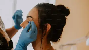 Mujer arreglando las cejas a otra