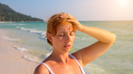 Chica en la playa con dolor de cabeza
