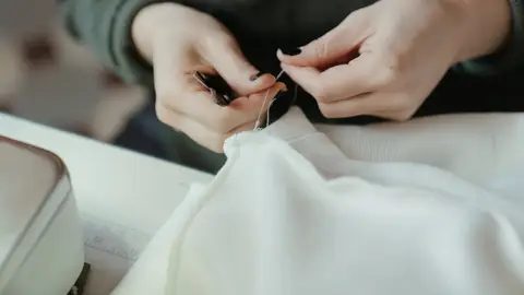 Manos de mujer arreglando una costura en una prenda de ropa Manos de mujer arreglando una costura en una prenda de ropa