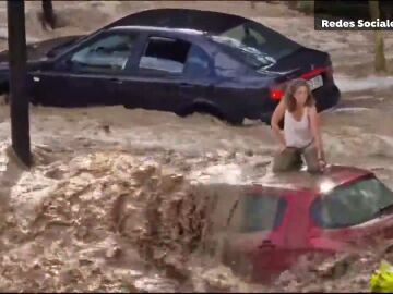 Una mujer resguardada del agua sobre su coche