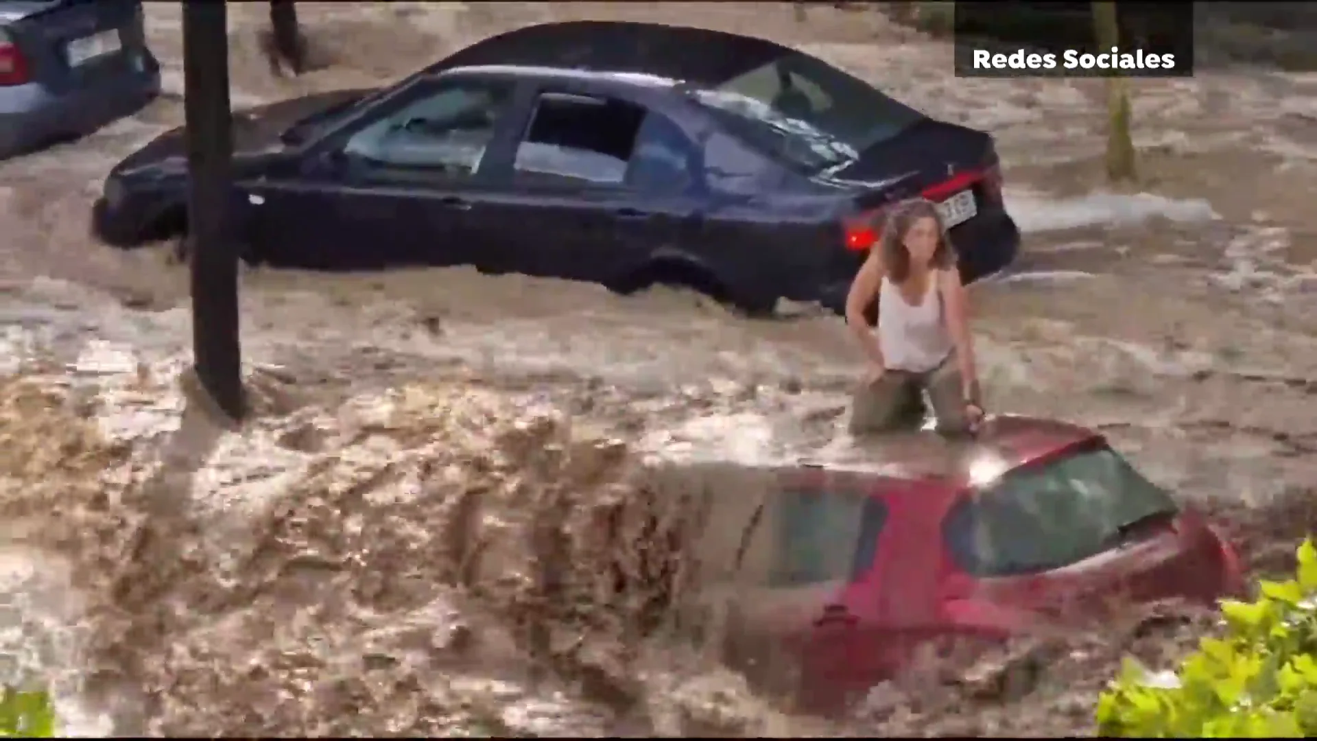 Una mujer resguardada del agua sobre su coche