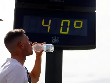 Un joven bebe agua junto a un termómetro de calle que marca 40 grados Un joven bebe agua junto a un termómetro de calle que marca 40 grados