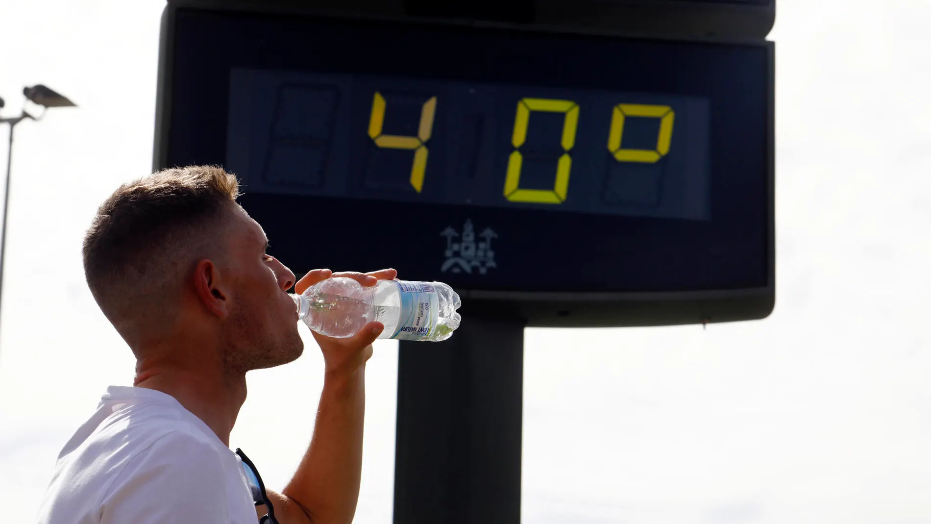 Un joven bebe agua junto a un termómetro de calle que marca 40 grados