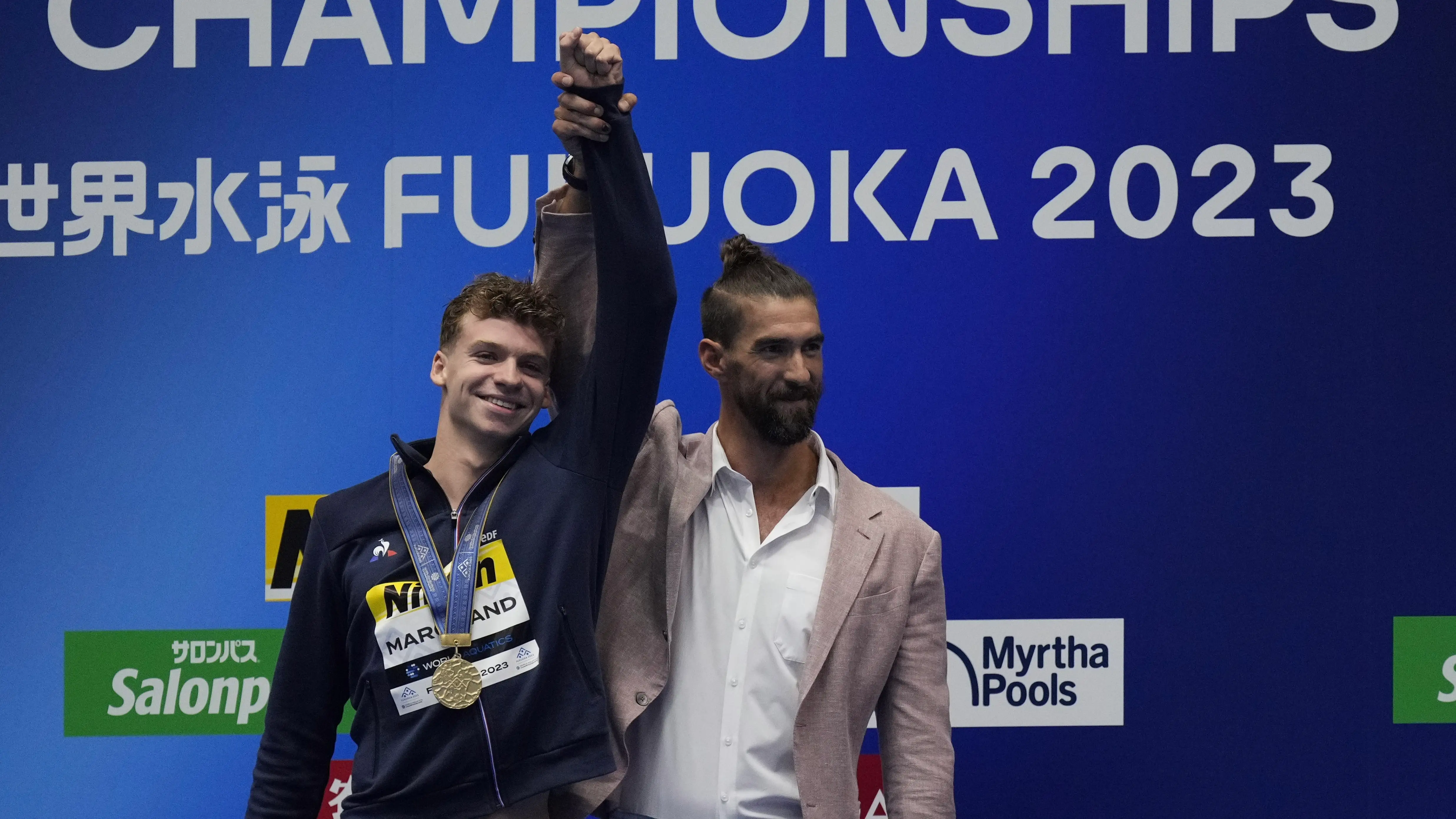 Michael Phelps levanta la mano del medallista de oro Léon Marchand Michael Phelps levanta la mano del medallista de oro Léon Marchand