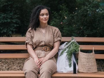 Mujer sentada en un banco de un parque con una bolsa de verduras