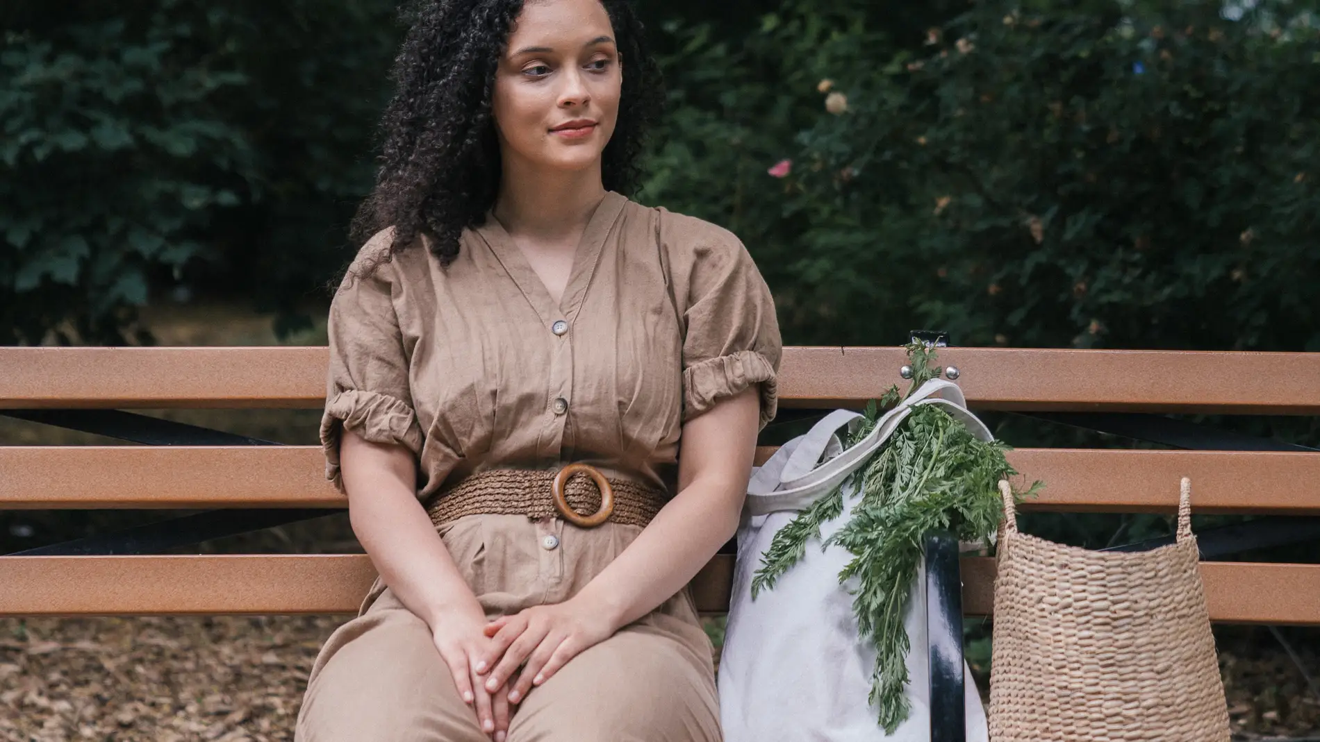 Mujer sentada en un banco de un parque con una bolsa de verduras