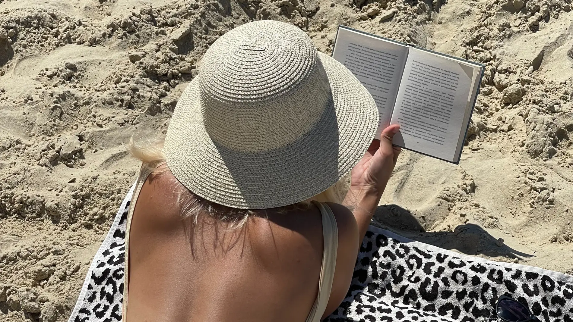 Mujer tumbada en la playa leyendo bajo el sol