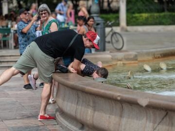 Un hombre refresca a su hijo en una fuente