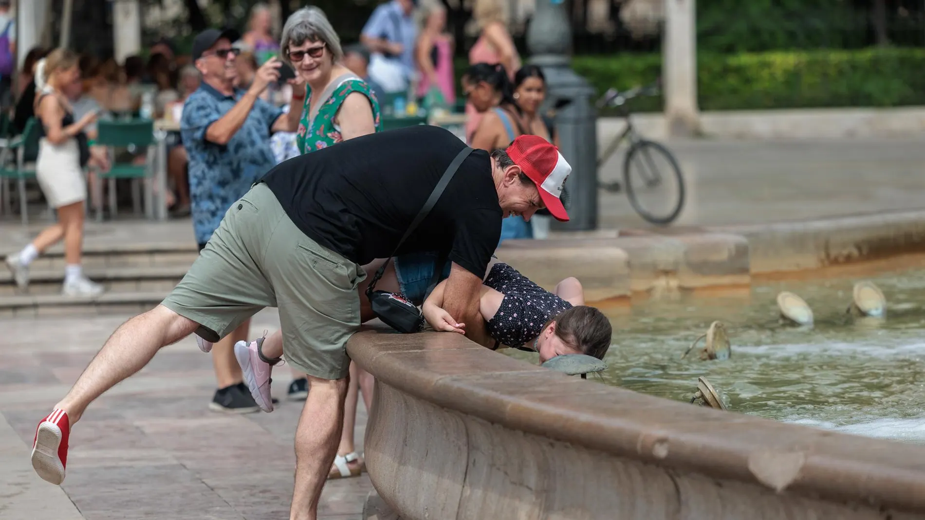 Un hombre refresca a su hijo en una fuente