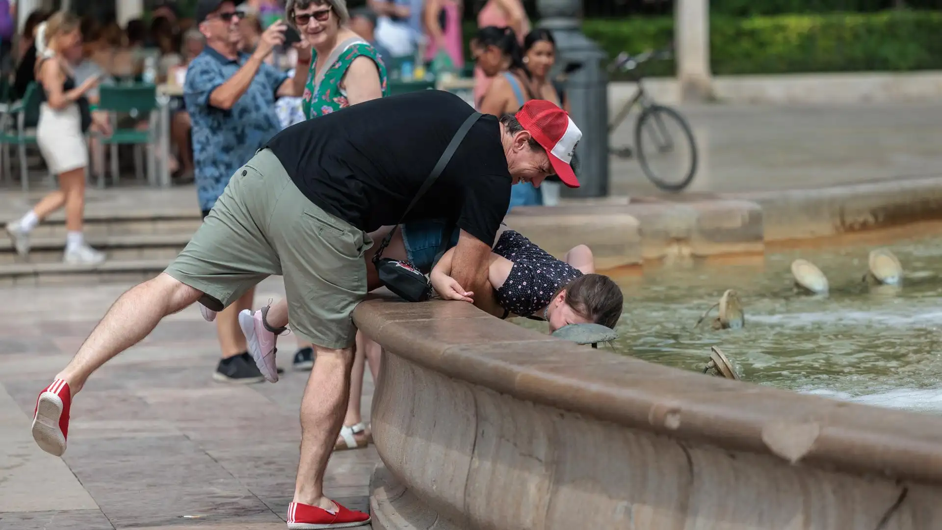 Un hombre refresca a su hijo en una fuente