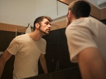 Un hombre se mira la piel del rostro en el espejo
