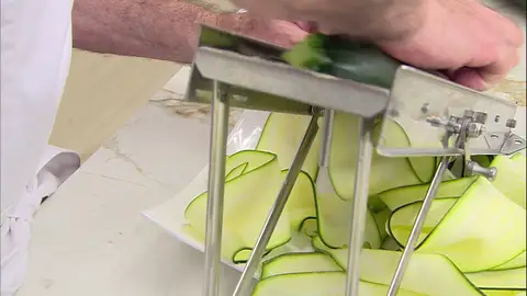Con una mandolina, lamina los dos calabacines Con una mandolina, lamina los dos calabacines