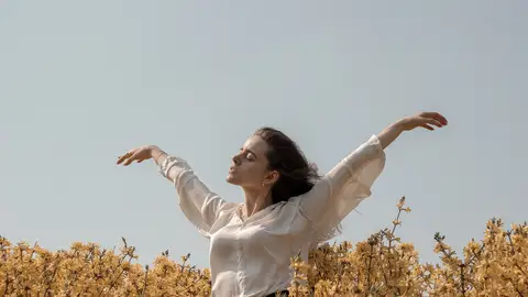 Mujer sintiendo el viento entre las flores del campo