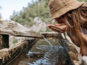 Una mujer bebe agua de una fuente en la naturaleza.