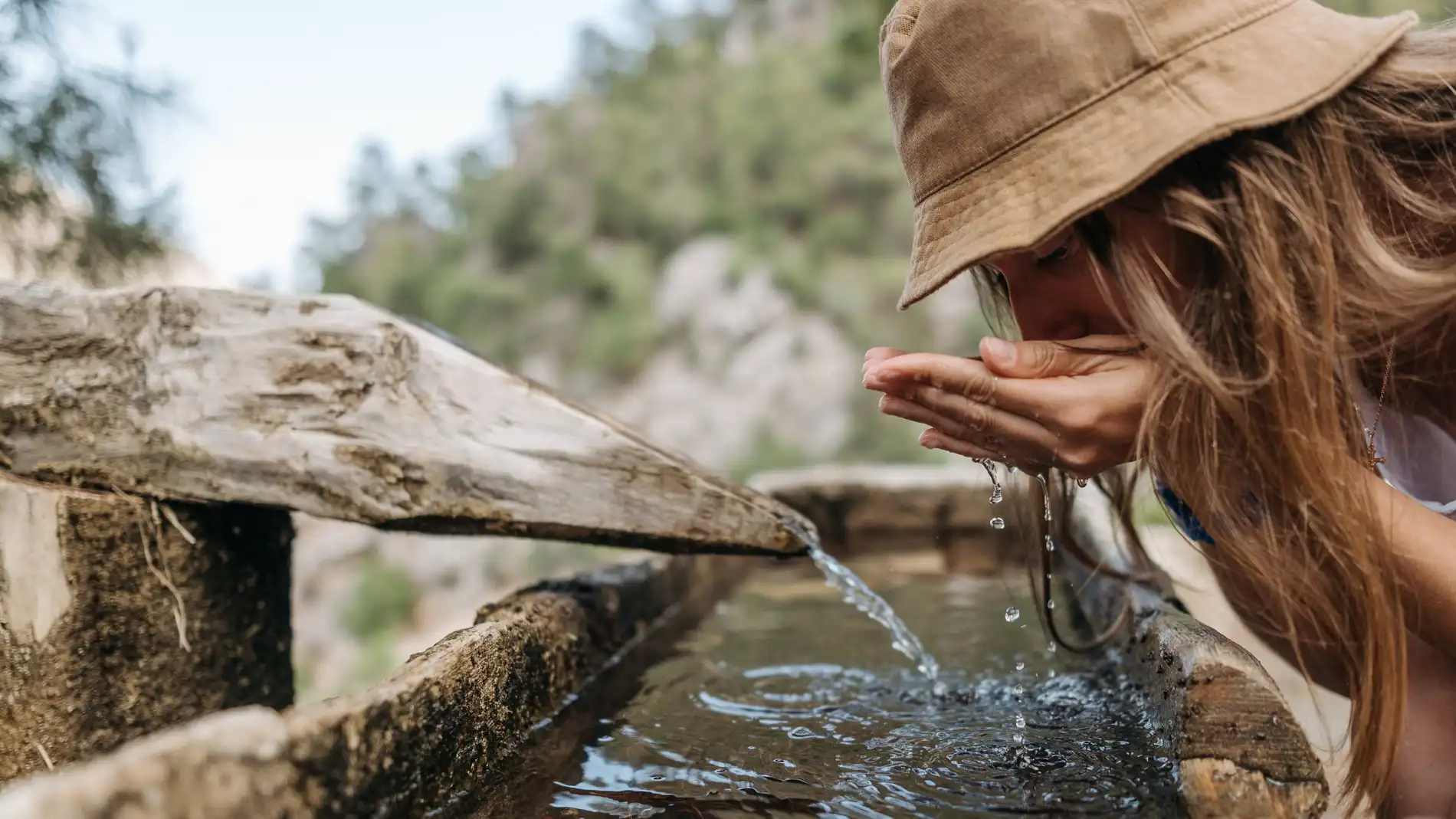 Una mujer bebe agua de una fuente en la naturaleza.